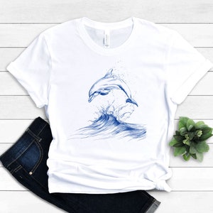May include: White t-shirt with a blue graphic of a dolphin jumping out of the water.