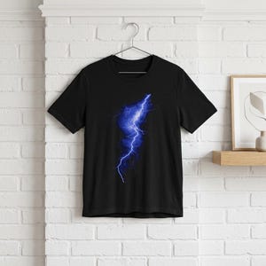 Puede incluir: Camiseta negra con un llamativo diseño de rayo azul. El diseño eléctrico azul está centrado en la camiseta. La camiseta está hecha de tela suave y tiene mangas cortas.