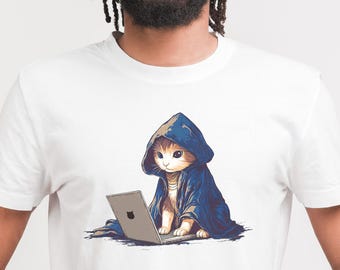 May include: White t-shirt featuring a cartoon illustration of a cat wearing a blue hooded cloak and using a laptop. The cat has orange and white fur and is sitting in front of the laptop. The laptop is silver with a black apple logo.