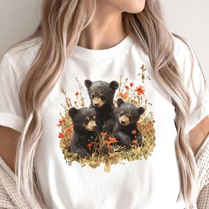 May include: White t-shirt with a graphic of three black bear cubs sitting in a field of flowers.