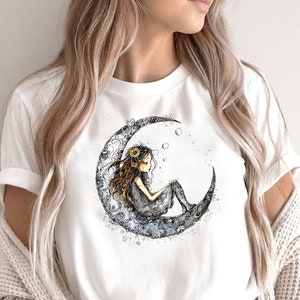 Könnte beinhalten: Weißes T-Shirt mit einem Motiv einer sitzenden Frau auf einem Halbmond mit einer Blumenkrone und Blasen um sie herum.