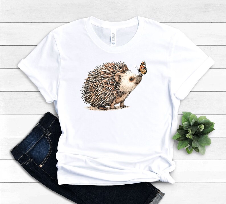 May include: White t-shirt with a brown and white hedgehog looking at an orange butterfly.