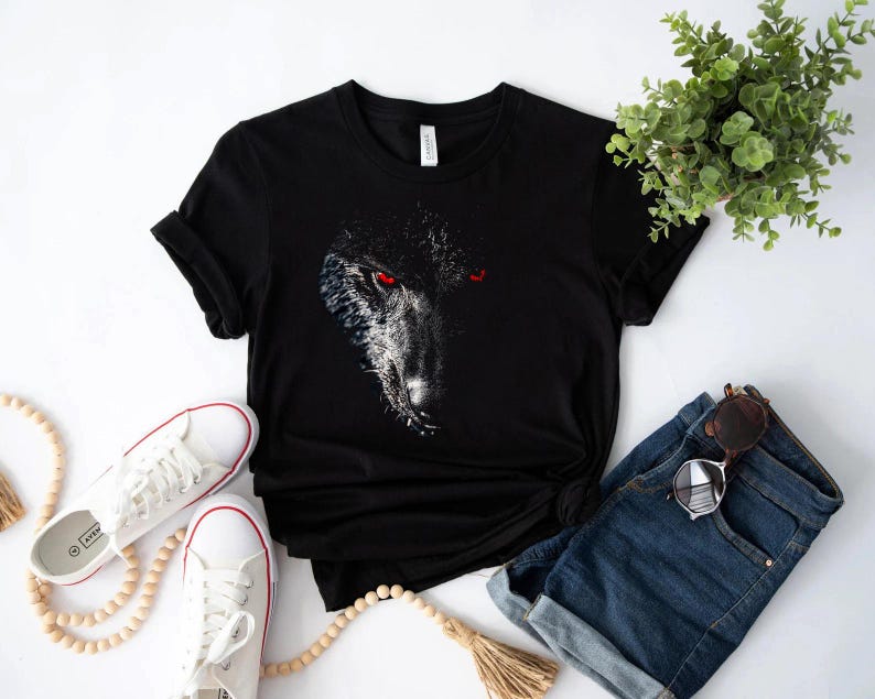 Puede incluir: Camiseta negra con un gr&aacute;fico de la cara de un lobo con ojos rojos. La cara del lobo est&aacute; en el centro de la camiseta y est&aacute; rodeada de un fondo negro.