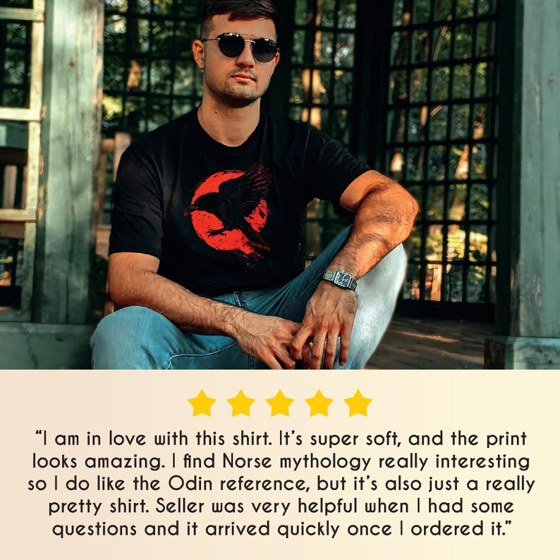 May include: Black t-shirt featuring a red graphic of a raven in front of a red circle. The shirt is worn by a person wearing sunglasses and a watch. The shirt design may be inspired by Norse mythology.