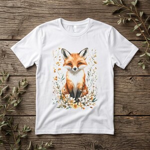 Puede incluir: Camiseta blanca con una ilustración de acuarela de un zorro rodeado de flores y follaje. El zorro tiene pelaje naranja y blanco, con nariz y orejas negras. Las flores son amarillas y blancas.