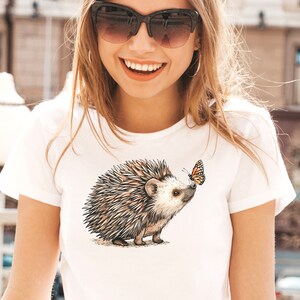 May include: White t-shirt with a brown and gray hedgehog and a yellow and orange butterfly graphic.