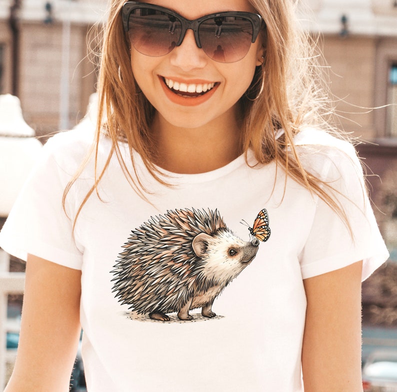 May include: White t-shirt with a brown and gray hedgehog and a yellow and orange butterfly graphic.