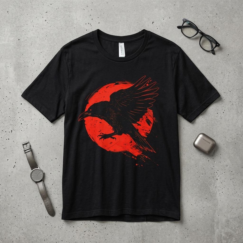 May include: Black t-shirt featuring a graphic of a black raven in flight against a red circle. The raven's wings are spread, and the design has a distressed, vintage look. The shirt is a crew neck style.