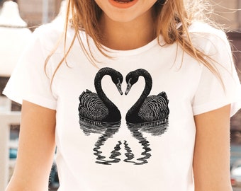 May include: A white t-shirt with a black and white illustration of two black swans facing each other with their necks forming a heart shape. The swans are reflected in the water below.