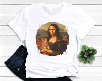 Peut inclure: T-shirt blanc avec un imprimé graphique de la Joconde tenant un chaton. Le graphique est de style vintage avec un fond délavé.
