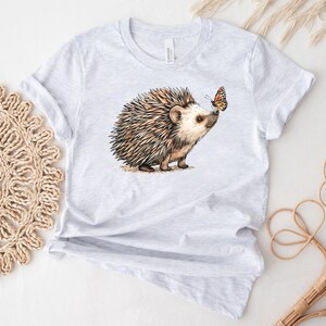 May include: A gray t-shirt with a brown and white hedgehog and a butterfly on it.