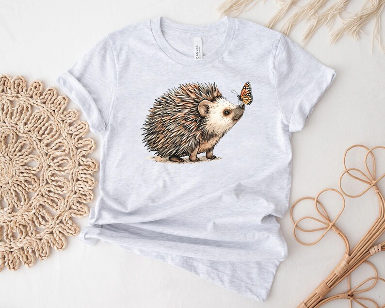 May include: A gray t-shirt with a brown and white hedgehog and a butterfly on it.