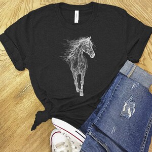 May include: Black t-shirt featuring a white, ethereal illustration of a horse. The horse design appears to be made of smoke or light. The shirt is paired with blue denim jeans and white sneakers, creating a casual, everyday look.