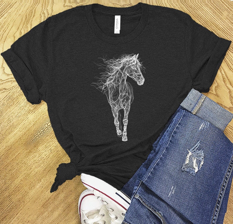 May include: Black t-shirt featuring a white, ethereal illustration of a horse. The horse design appears to be made of smoke or light. The shirt is paired with blue denim jeans and white sneakers, creating a casual, everyday look.