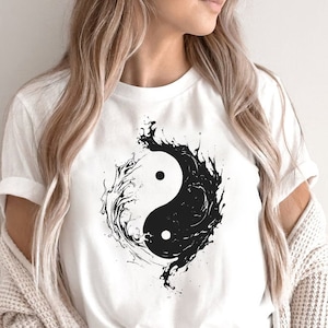 以下が含まれることがあります： 白地に黒と白の陰陽のシンボルデザインが施されたTシャツ。シンボルは、水を思わせる渦巻き模様で囲まれています。