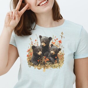May include: A light blue t-shirt with a graphic of three black bear cubs surrounded by red flowers and green foliage.