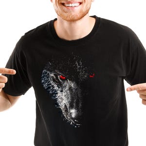 Puede incluir: Una camiseta negra con un estampado gr&aacute;fico de la cara de un lobo con ojos rojos.