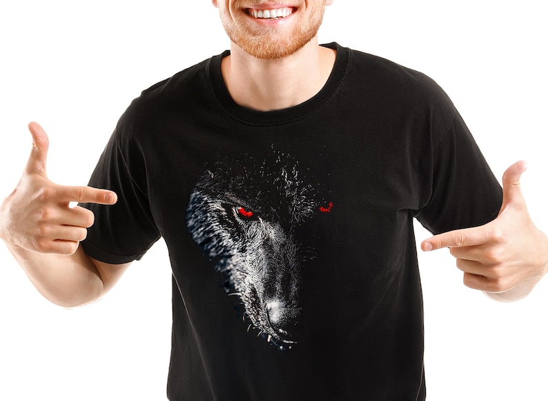 Puede incluir: Una camiseta negra con un estampado gr&aacute;fico de la cara de un lobo con ojos rojos.