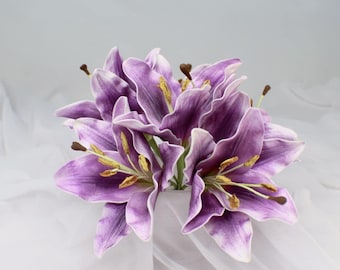 May include: A cluster of purple lily flowers with white edges and yellow stamens. The petals are a deep purple with white edges, and the stamens are yellow. The flowers are arranged in a bouquet, with green stems.
