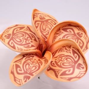 May include: Close-up of a faux plumeria flower with five petals. The petals are a light orange colour with a brown tribal design. The flower is a tropical theme.