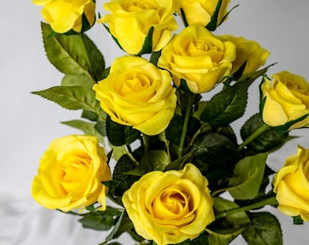Pode incluir: Um buquê de rosas amarelas com folhas verdes. As rosas estão dispostas em um vaso, e os caules são visíveis.