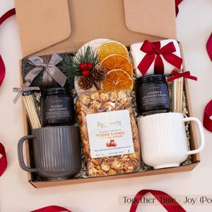 Luxurious holiday gift box for couples featuring gray and white ribbed mugs, caramel popcorn, pinecone and dried orange decor, cozy socks, and festive red ribbons — a warm and modern Christmas gift set.