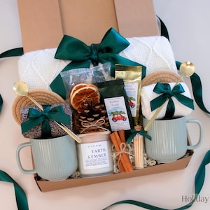 Rustic winter gift box in spruce green with ceramic mugs, cinnamon sticks, dried oranges, pinecones, and seasonal coffee — a festive and earthy holiday gift set for couples.