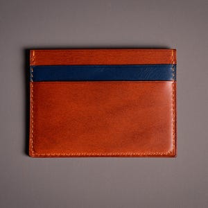 Porte-cartes rectangulaire en cuir marron et bleu marine. Le porte-cartes a un aspect riche et texturé avec une bande bleu marine sur le dessus. Les bords sont cousus avec un fil contrastant.