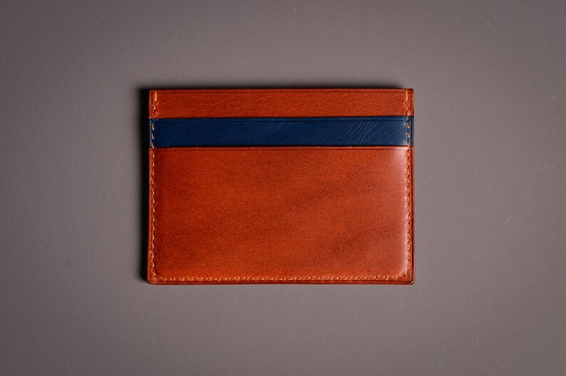 Porte-cartes rectangulaire en cuir marron et bleu marine. Le porte-cartes a un aspect riche et texturé avec une bande bleu marine sur le dessus. Les bords sont cousus avec un fil contrastant.