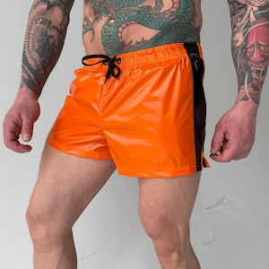 May include: Bright orange swim trunks with a black side panel and a drawstring waist. The shorts have a shiny, reflective finish. The overall theme is swimwear.