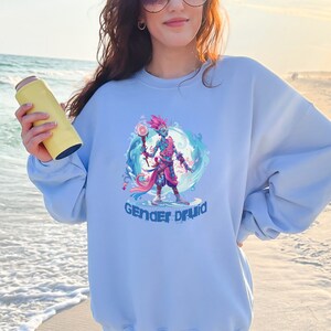 May include: Light blue sweatshirt with a graphic of a blue and pink humanoid figure holding a staff, surrounded by water and flowers. The text "Gender Druid" is printed below the figure.