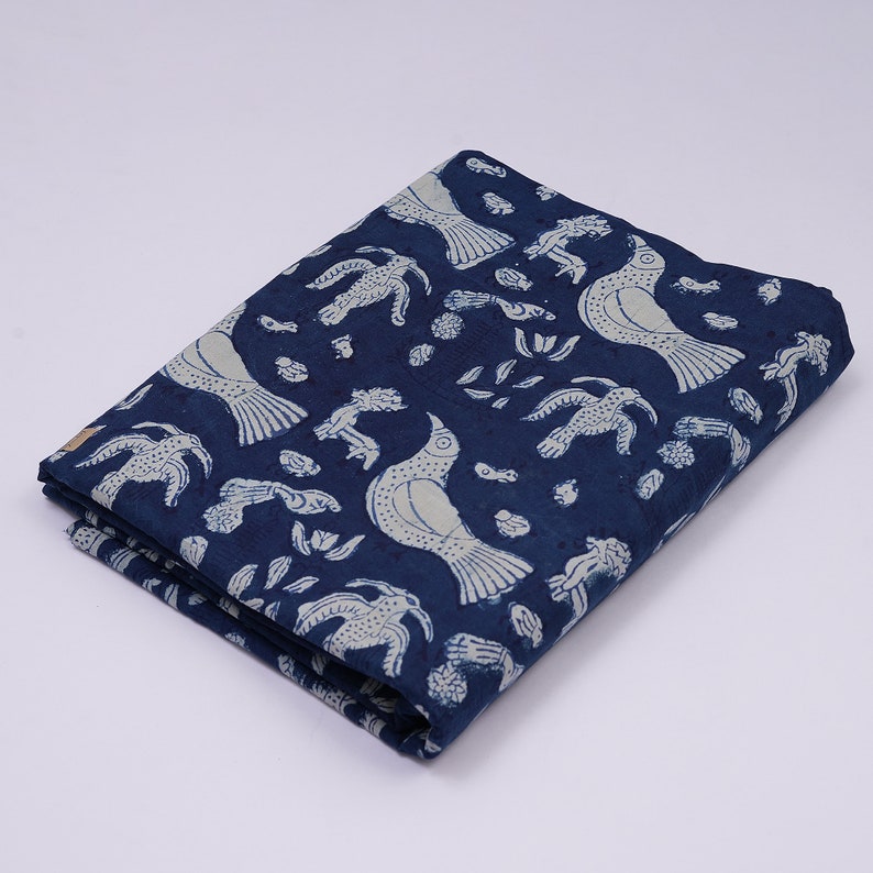 Peut inclure: Un tissu en coton bleu avec un motif de fleurs et d'oiseaux blancs. Le tissu est pli&eacute; en deux et a une surface textur&eacute;e.