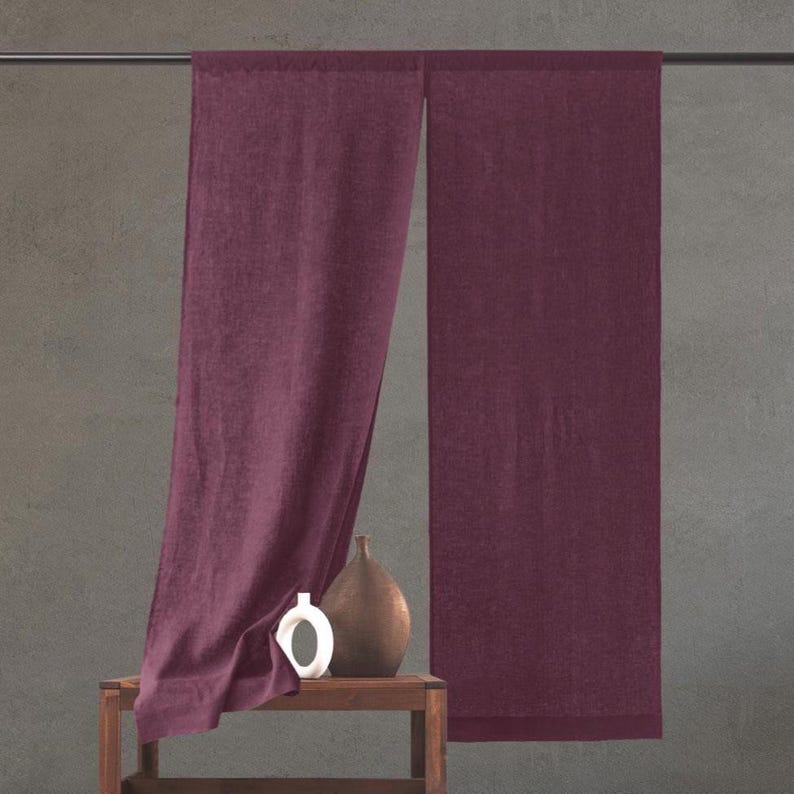 A minimalist deep green Noren-style curtain hangs from a sleek rod, featuring two panels with a central split. The rich fabric drapes softly, complementing the neutral wall and modern decor, with a small potted plant adding a fresh touch.