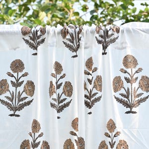 Peut inclure: Un rideau blanc orné d'un motif imprimé répétitif de fleurs marron et beige. Le tissu présente une tête froncée et affiche une série de tiges florales symétriques avec des feuilles détaillées et des fleurs arrondies et texturées.