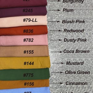 Puede incluir: Una pila de muestras de tela en varios colores, incluyendo borgo&ntilde;a, ciruela, rosa rubor, secuoya, rosa polvoriento, marr&oacute;n coca, mostaza, verde oliva, canela y azul denim claro. Cada muestra est&aacute; etiquetada con un nombre de color y un n&uacute;mero.