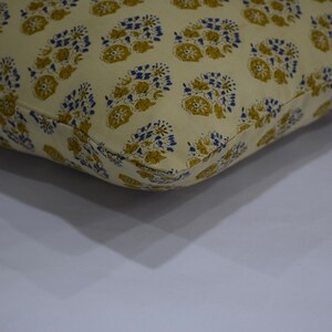 Pode incluir: Uma almofada de cor creme com um padr&atilde;o floral em tons de amarelo e azul. A almofada &eacute; feita de algod&atilde;o e tem um design simples e elegante.