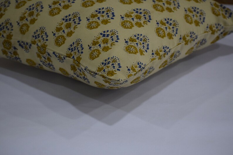 Pode incluir: Uma almofada de cor creme com um padr&atilde;o floral em tons de amarelo e azul. A almofada &eacute; feita de algod&atilde;o e tem um design simples e elegante.