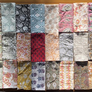 May include: A collection of twenty-four rectangular fabric napkins arranged in a grid, featuring a variety of block-printed patterns including floral, paisley, geometric, and botanical designs in diverse colors like pink, yellow, blue, and grey.