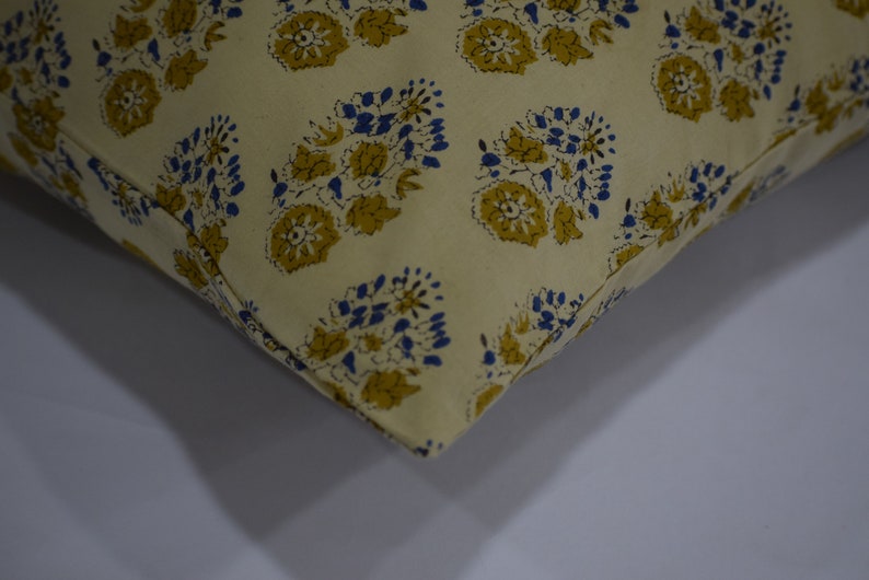 Pode incluir: Close-up de uma almofada de cor creme com um padr&atilde;o floral azul e amarelo. A almofada &eacute; feita de um tecido macio e texturizado.