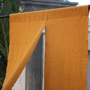 Peut inclure: Un rideau noren jaune moutarde avec un design fendu suspendu à une tringle noire. Le tissu présente une texture tissée visible et une couleur unie uniforme, avec un bord ourlé net le long de l'ouverture verticale et de la poche à tringle.