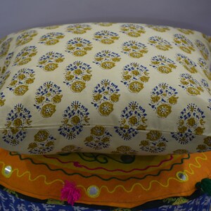 Pode incluir: Uma almofada de cor creme com um padr&atilde;o floral em tons de amarelo e azul. A almofada est&aacute; colocada em cima de um coj&iacute;n colorido com padr&atilde;o.