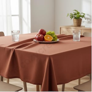 Puede incluir: Un mantel de color &oacute;xido cubre una mesa de madera, con dos vasos estampados y un plato de fruta. La fruta incluye manzanas rojas, uvas verdes y media naranja. Una peque&ntilde;a planta en maceta se encuentra en el fondo.