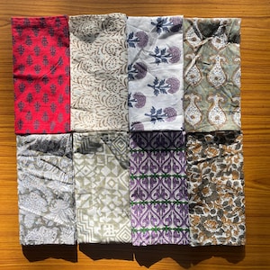 May include: A collection of eight rectangular fabric napkins arranged in two rows. The patterns include red with dark grey trees, beige with swirling vines, white with purple floral sprigs, olive green with paisley, grey floral, geometric beige, purple paisley, and floral brown.