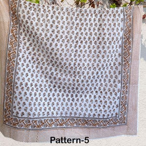 K&ouml;nnte beinhalten: Wei&szlig;er Baumwollstoff mit braunem Blumenmuster. Der Stoff hat einen braunen Rand mit einem sich wiederholenden Blumenmuster. Der Stoff ist mit "Pattern-5" gekennzeichnet.