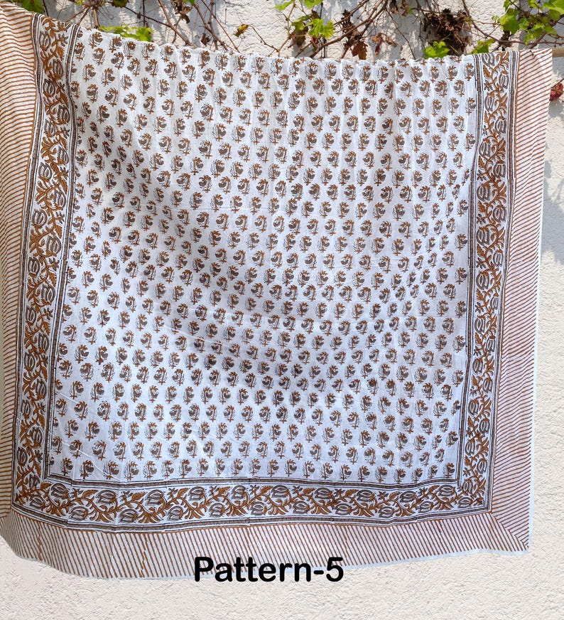 K&ouml;nnte beinhalten: Wei&szlig;er Baumwollstoff mit braunem Blumenmuster. Der Stoff hat einen braunen Rand mit einem sich wiederholenden Blumenmuster. Der Stoff ist mit "Pattern-5" gekennzeichnet.