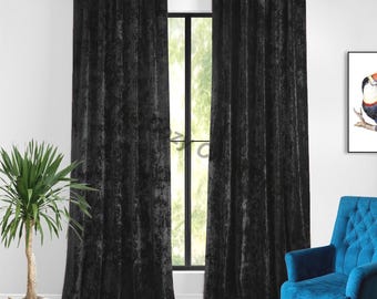 May include: Two black velvet curtains hang on a silver rod, framing a window with a view of greenery. A potted plant sits to the left, and a blue armchair is on the right. A framed bird art piece hangs on the wall.