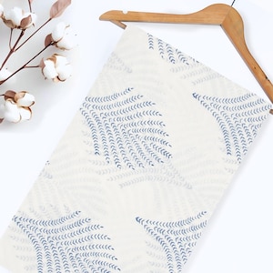 May include: White fabric with a blue and white pattern of stylized leaves. The fabric is hanging on a wooden hanger.