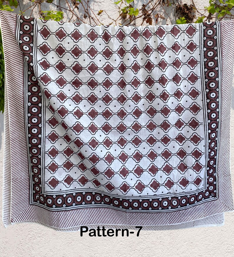 K&ouml;nnte beinhalten: Wei&szlig;er Baumwollstoff mit braunem geometrischem Muster. Der Stoff hat einen Rand mit einem sich wiederholenden Muster aus Kreisen und Streifen. Der Stoff ist mit "Pattern-7" gekennzeichnet.