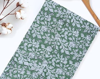 May include: A green fabric with a white floral pattern. The fabric is hanging on a wooden hanger.