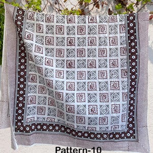 K&ouml;nnte beinhalten: Wei&szlig;er Baumwollstoff mit einem braunen und schwarzen geometrischen Muster. Der Stoff hat einen Rand mit einem sich wiederholenden Kreisdesign. Der Stoff ist mit "Pattern-10" gekennzeichnet.